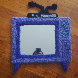 A tufted hand-made rug mirror of a purple antenna tv.
