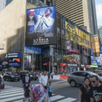A street corner view in Manhattan of the A digital banner featuring an animated stage graphic promoting the 2019 SummerStage season at the Playstation Theater in NY