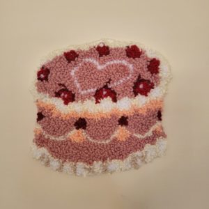 A tufted hand-made rug of an ornate pink cake.